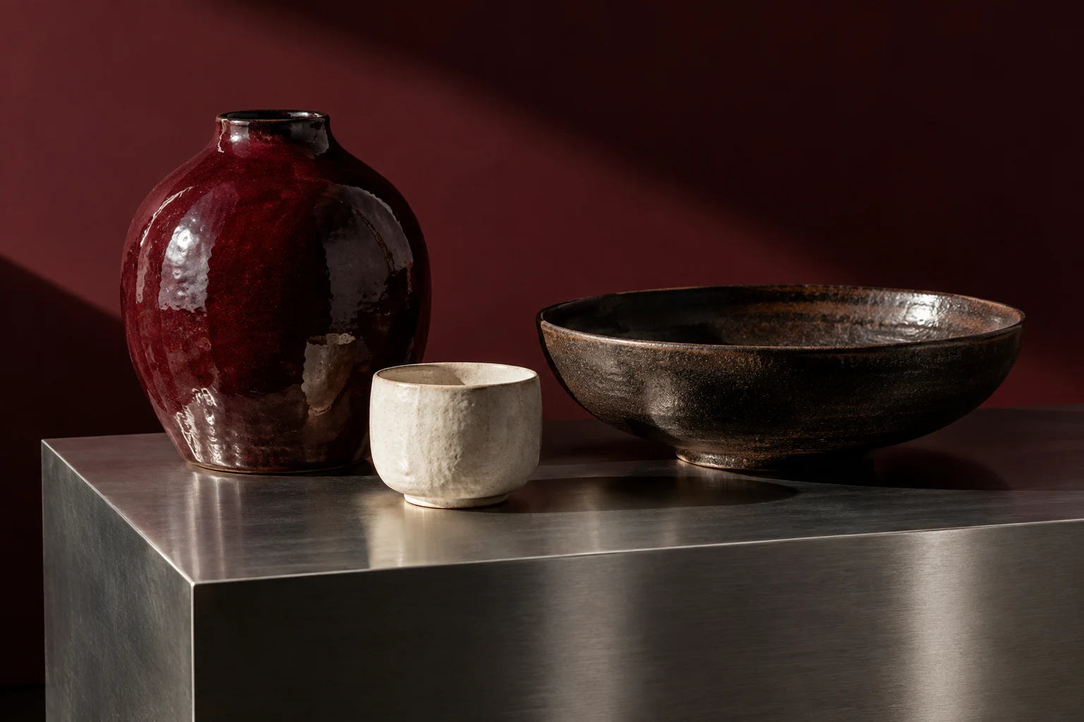 AI-generated oxblood vase, chalk cup and dark bowl on steel; fictional products